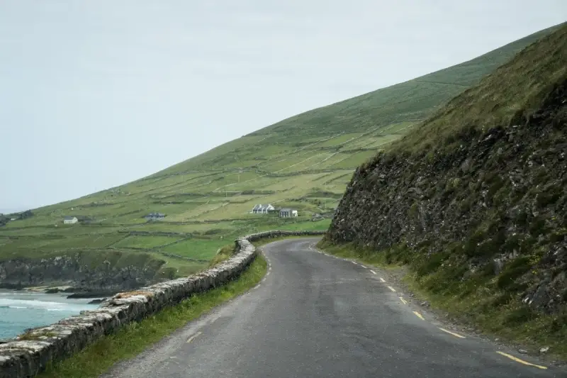A winding road along the coast of Ireland, perfect for renting a car and exploring the dramatic green hills and stone walls.