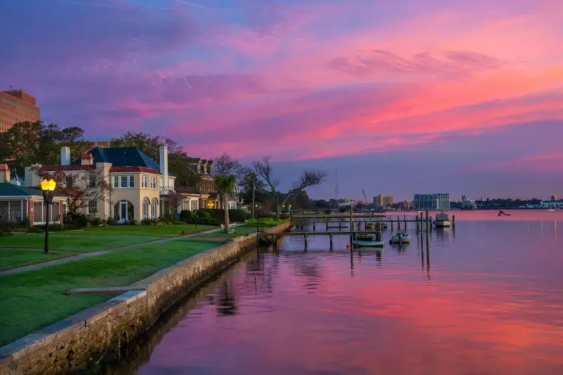 Beautiful waterfront homes and boats reflect a vibrant pink and purple sunset, perfect for weekend trips from Richmond, VA.